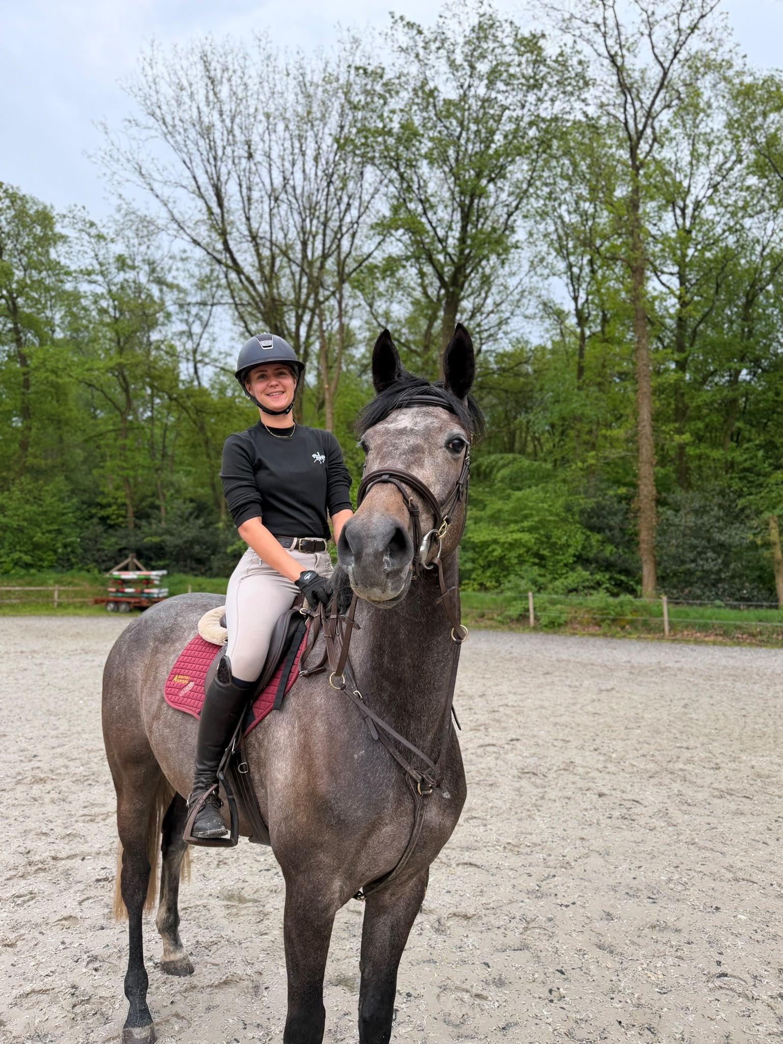 Lynn Bouwmeester zit glimlachend op haar schimmel in de buitenbak.